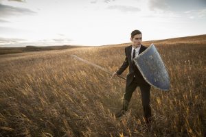 Alert businessman with sword and shield outdoors