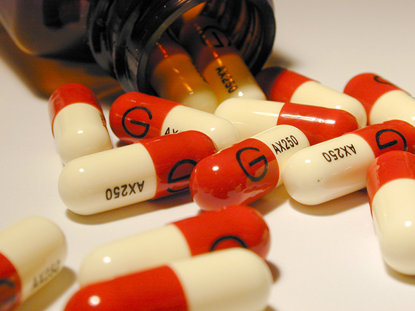 Red and white antibiotic capsules spilling out of a bottle onto a white surface in a medical and healthcare concept